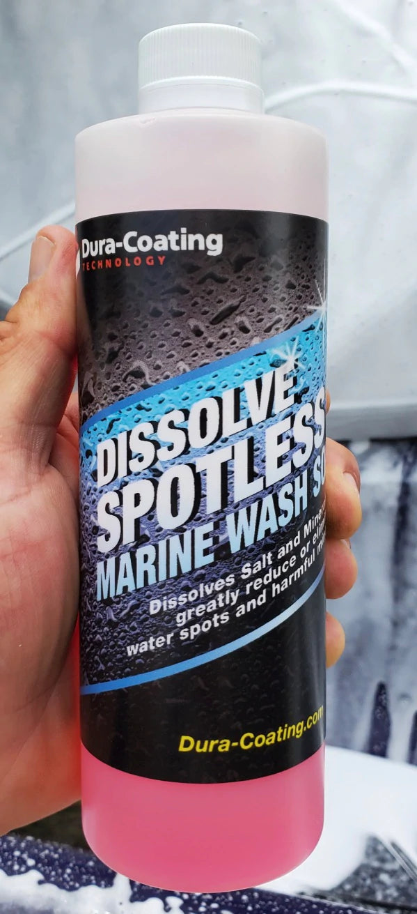 16 oz bottle Dura-Coating Dissolve Spotless Marine Wash, mans left hand holding bottle palm toward viewer, thumb up. Soapy image blurry in background.